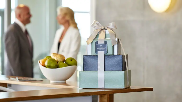 A photo of corporate gifting for the new year with a gift tower on a counter next to a bowl of pears with two people talking in the background.
