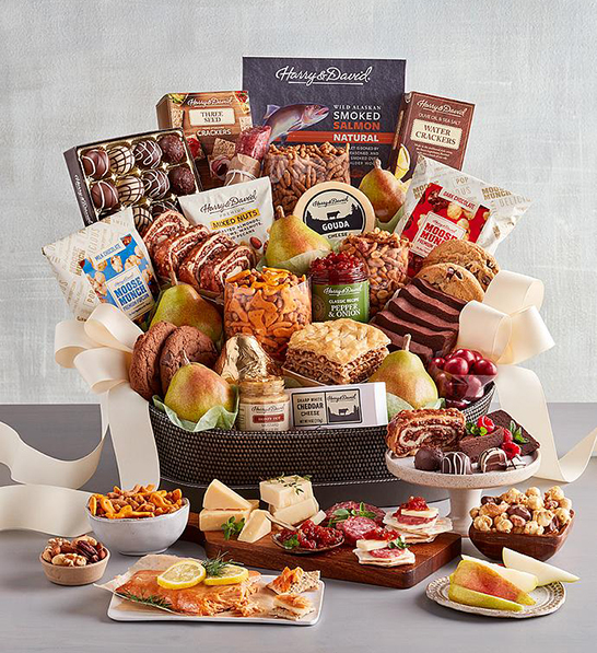 A photo of corporate gifting for the new year with a box full of chocolate, cookies, fruit, cheese and meats with the same ingredients arrayed in front of the box on cutting boards and plates.