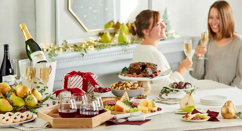 A photo of facts about Christmas with a spread of food, wine and gifts with two women drinking and talking in the background.