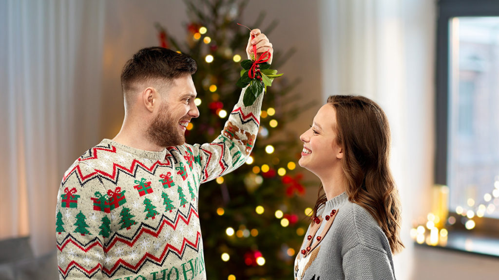 A photo of facts about Christmas with a man and a woman standing opposite one another with the man holding a bundle of mistletoe about their heads.