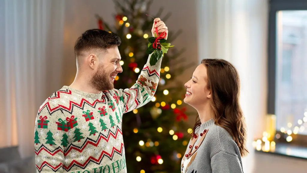 A photo of facts about Christmas with a man and a woman standing opposite one another with the man holding a bundle of mistletoe about their heads.