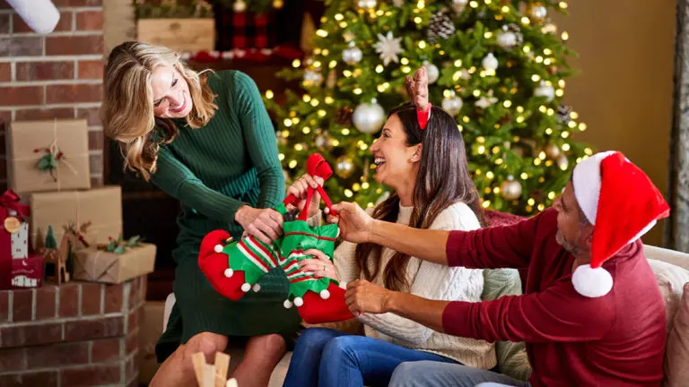 A photo of facts about Christmas with three people pulling at a Christmas gift while sitting on a couch and laughing