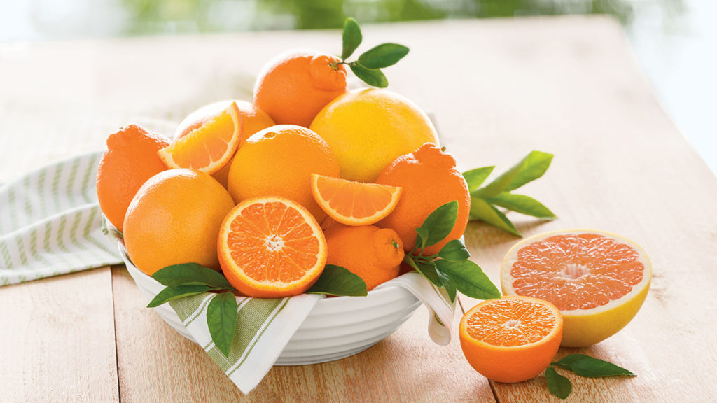 A photo of facts about oranges with a bowl of sliced and whole oranges on a table