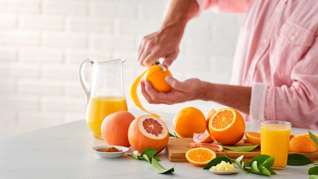 A photo of facts about oranges with someone peeling an orange with several sliced oranges in front of them along with a pitcher of orange juice.