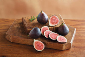 A photo of healthy fruit with whole and sliced figs on a wooden cutting board