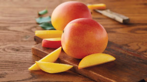 A photo of healthy fruit with two mangoes on a wooden board with a few slices of mango surrounding them