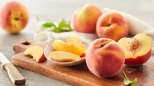 A photo of healthy fruit with several whole and sliced peaches on a cutting board