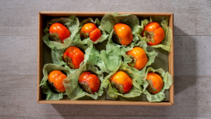 A photo of healthy fruit with a box of persimmons surrounded by green tissue paper.