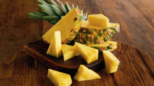 A photo of healthy fruit with several slices of pineapple on a wooden cutting board.