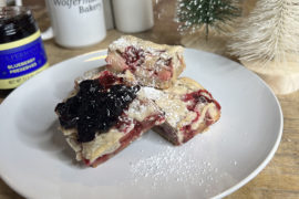 A photo of cobbler on a plate surrounded by a jar of preserves and a mug