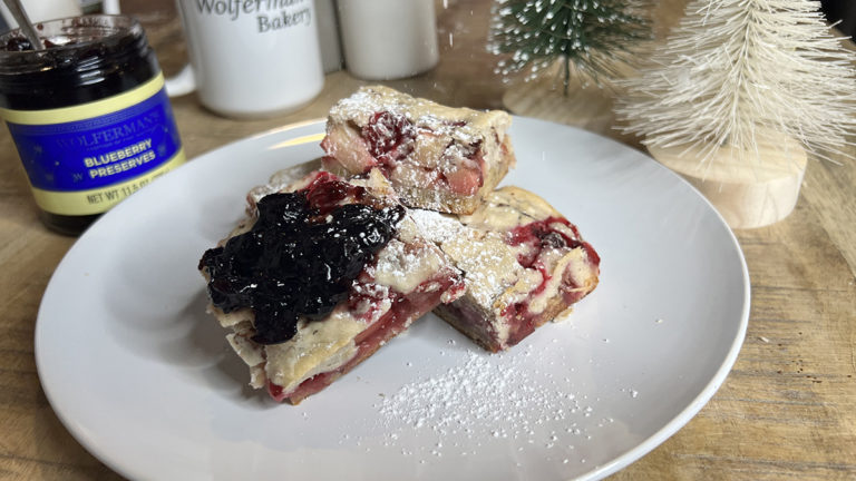 A photo of cobbler on a plate surrounded by a jar of preserves and a mug