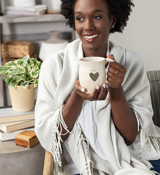 A photo of holiday gifts for employees with a woman wrapped in a blanket and holding a mug.