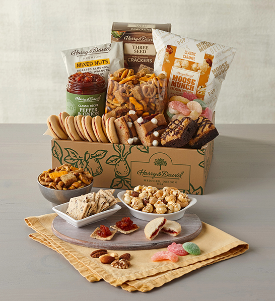 A photo of holiday gifts for employees with a box of sweet and savory snacks with a tray of the same ingredients in front of the box.
