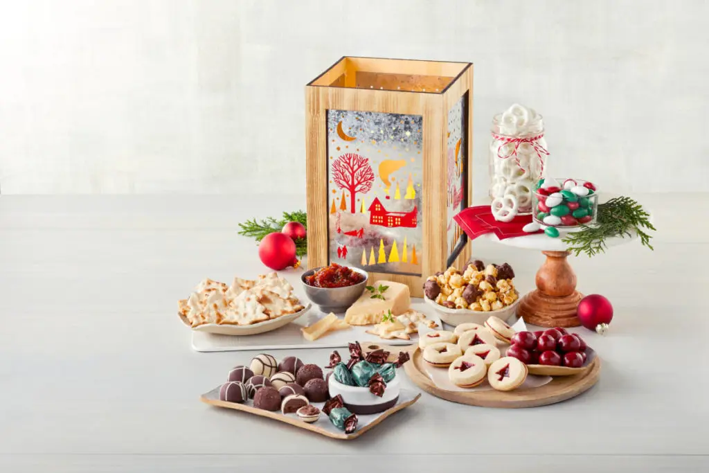 A photo of a holiday lantern surrounded by cookies, cheese, crackers and truffles