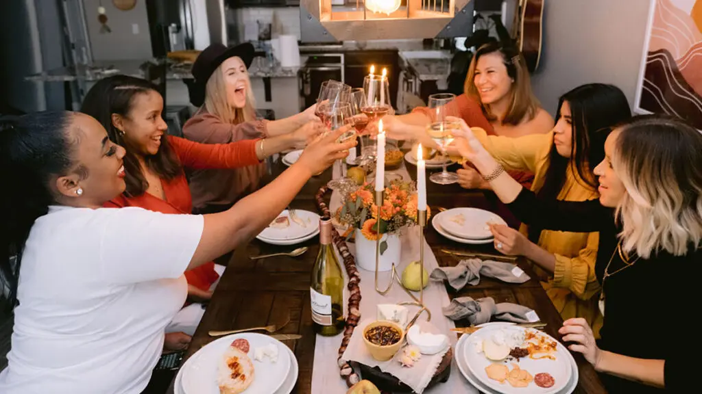 How to celebrate Kwanzaa with a group of women raising glasses at a table.