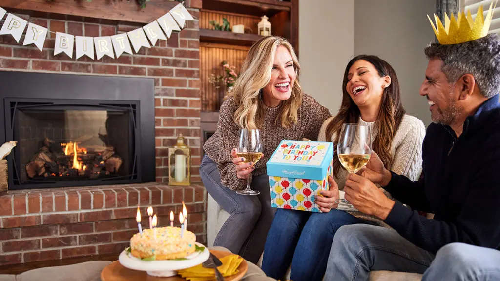 A photo of January birthdays with three people on a couch laughing and celebrating a birthday.