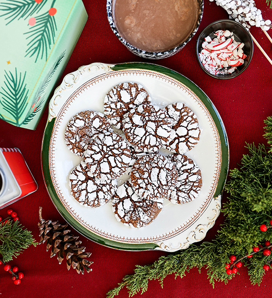 A photo of last minute gifts with a plate of chocolate crinkle cookies surrounded by greenery and crushed peppermint.