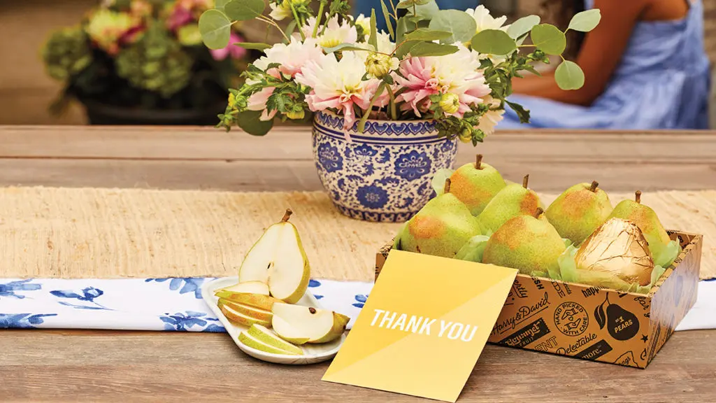 A photo of what to write in a thank you card with a box of pears with a thank you note in front and a plate of sliced pears