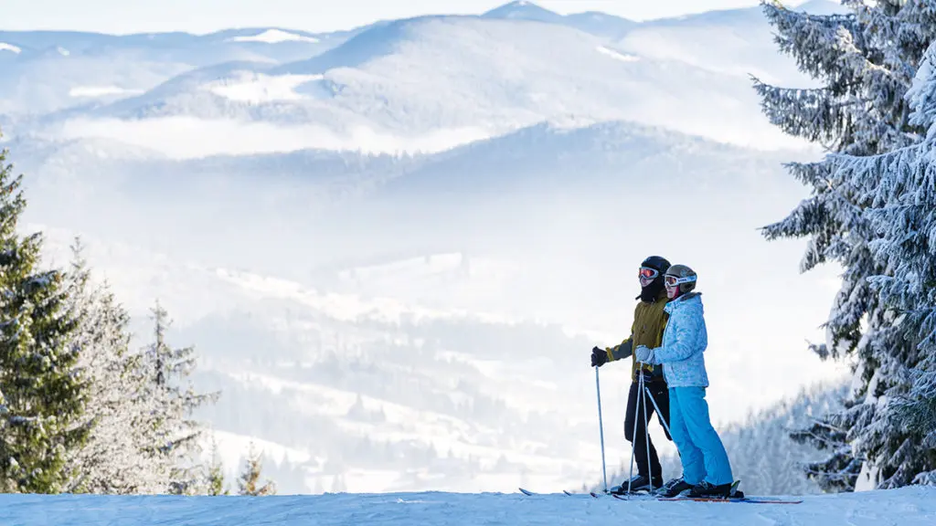 A photo of après ski with two people on skis in the snow with a mountain landscape in the background.