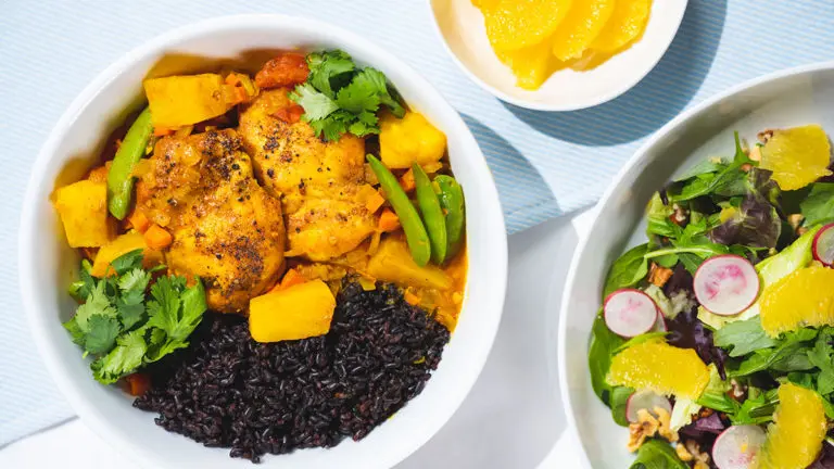 A photo of a curry recipe with two bowls on a counter, one full of rice and curry the other full of salad