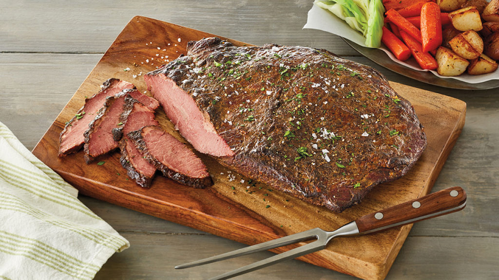 A photo of cuts of beef with a cooked brisket sitting on a cutting board with a few slices in front of it.