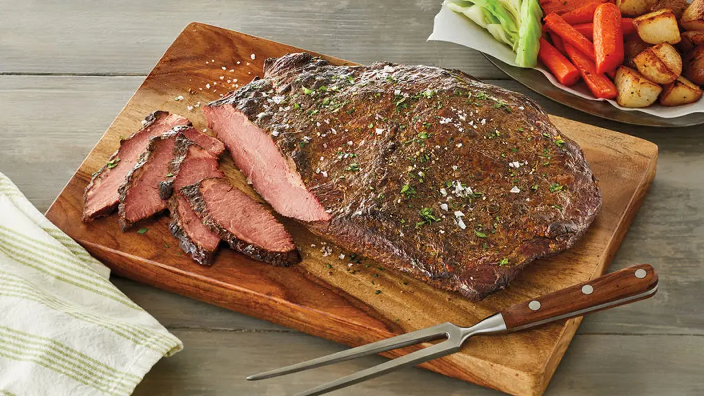 A photo of cuts of beef with a cooked brisket sitting on a cutting board with a few slices in front of it.