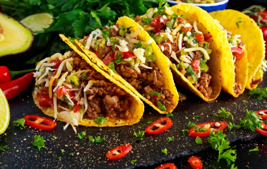 A photo of cuts of beef with a plate of tacos full of ground beef and other ingredients.