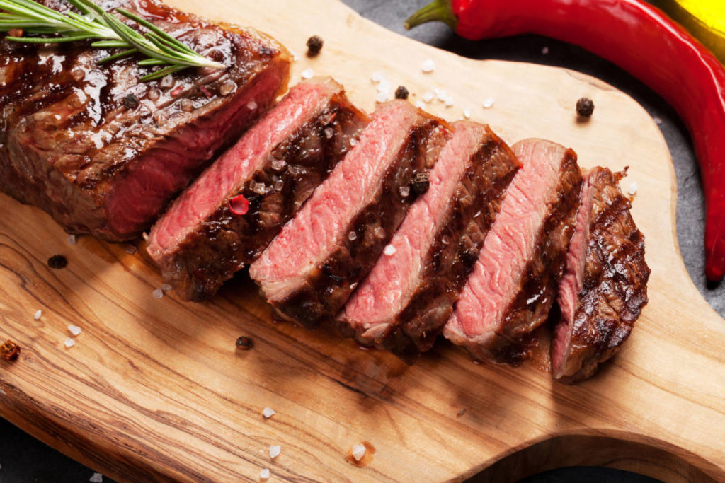 A photo of cuts of beef with a cutting board supporting a cooked and sliced sirloin steak.