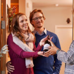 A photo of gifts for couples with a man and a woman accepting a bottle of wine from another woman