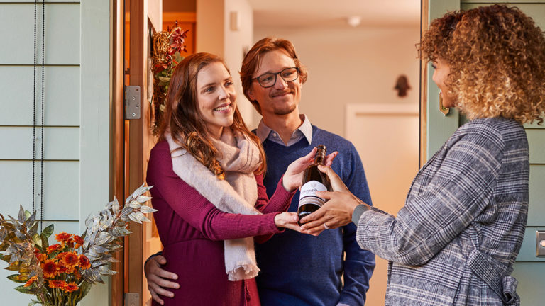 A photo of gifts for couples with a man and a woman accepting a bottle of wine from another woman