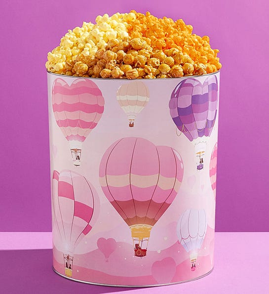 A photo of gifts for couples with a tin of flavored popcorn with heart shaped hot air balloons painted on the side of it.