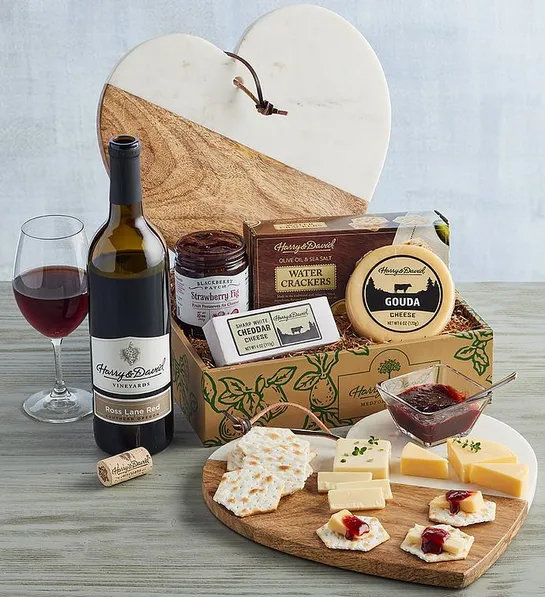 Gifts for couples with a box full of cheese, crackers and a heart shaped cheese board next to a bottle of wine.