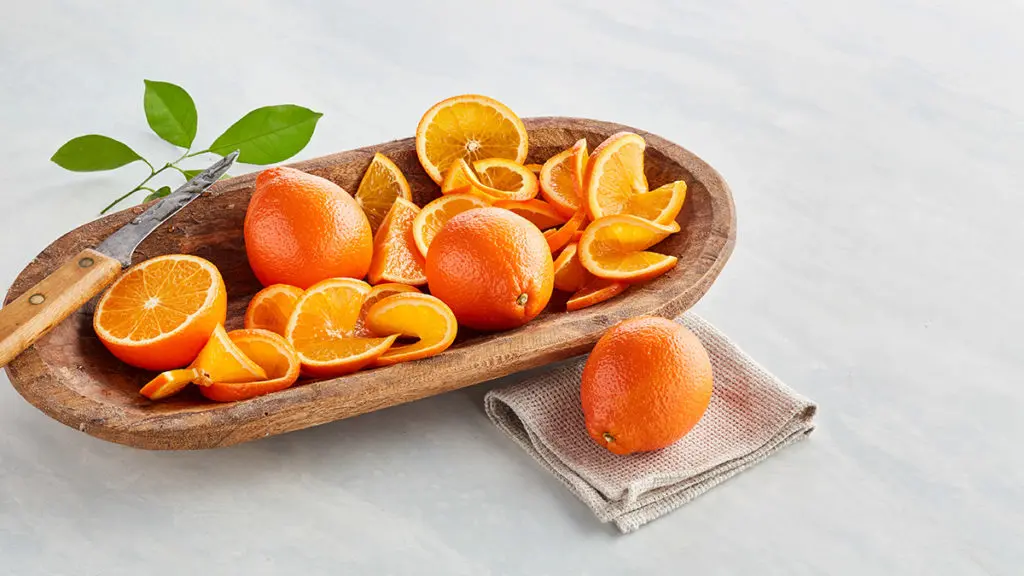 A photo of honeybell oranges, whole and sliced, in a wooden bowl.