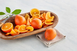 A photo of honeybell oranges, whole and sliced, in a wooden bowl.