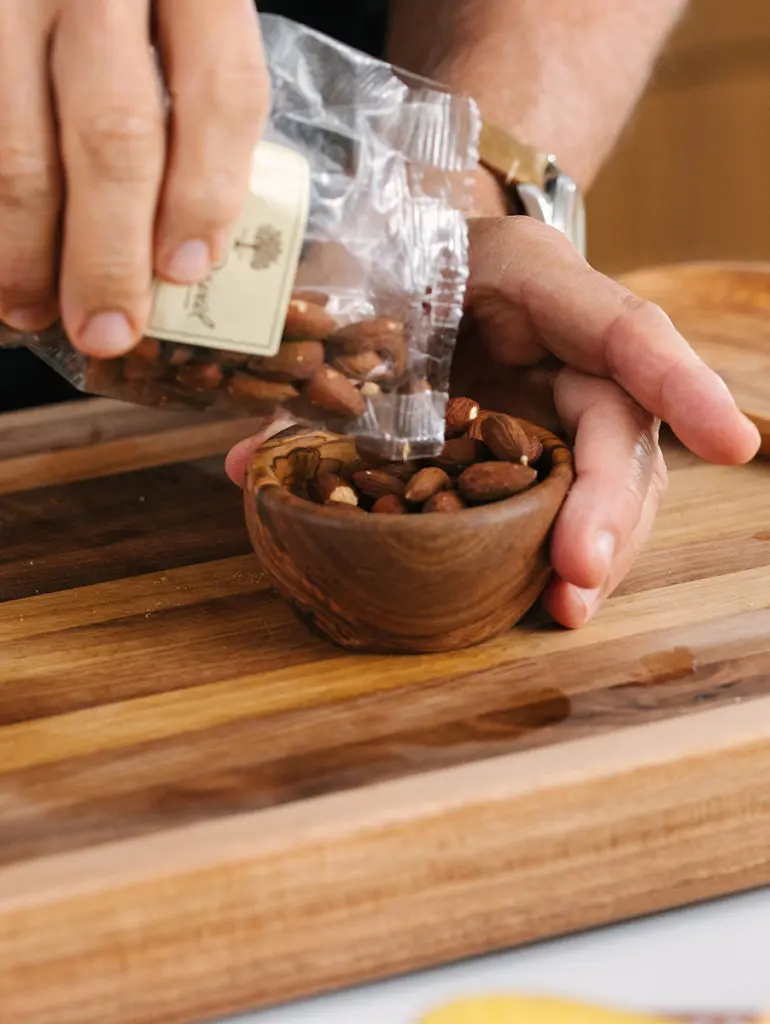 A photo of birthday charcuterie board with a closeup of Geoffrey Zakarian pouring almonds into a small wooden ramekin