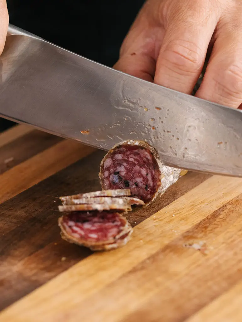 A photo of birthday charcuterie board with a closeup of Geoffrey Zakarian slicing salami