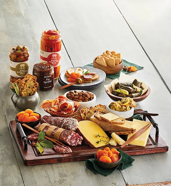 A photo of gifts for women with an array of cheese, meat and crackers on a board with the same ingredients sitting in bowls and jars next to it.