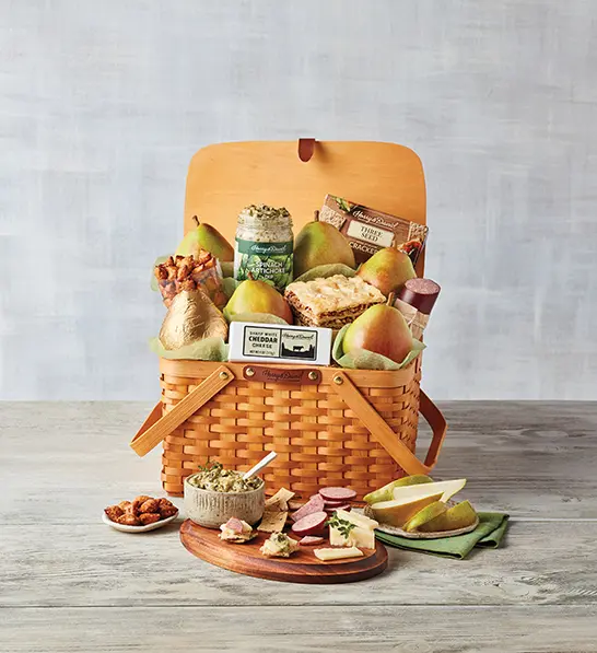 A photo of gifts for women with a picnic basket full of fruit, crackers, cheese, meat, and spreads with the same ingredients on a plate in front of the basket.