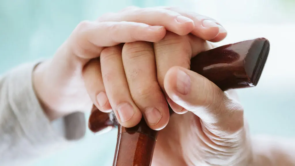 Photo of a caregiver's hand helping an elderly person with a cane