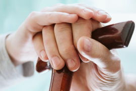 Photo of a caregiver's hand helping an elderly person with a cane