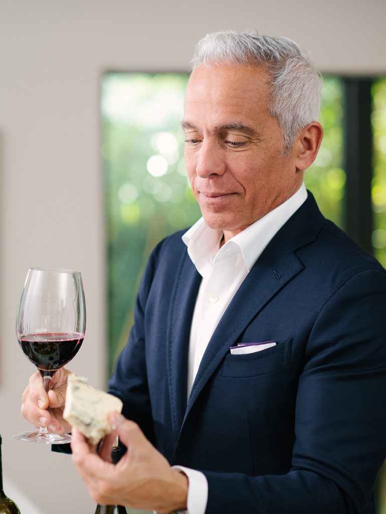 A photo of Geoffrey Zakarian holding a glass of wine and a hunk of cheese