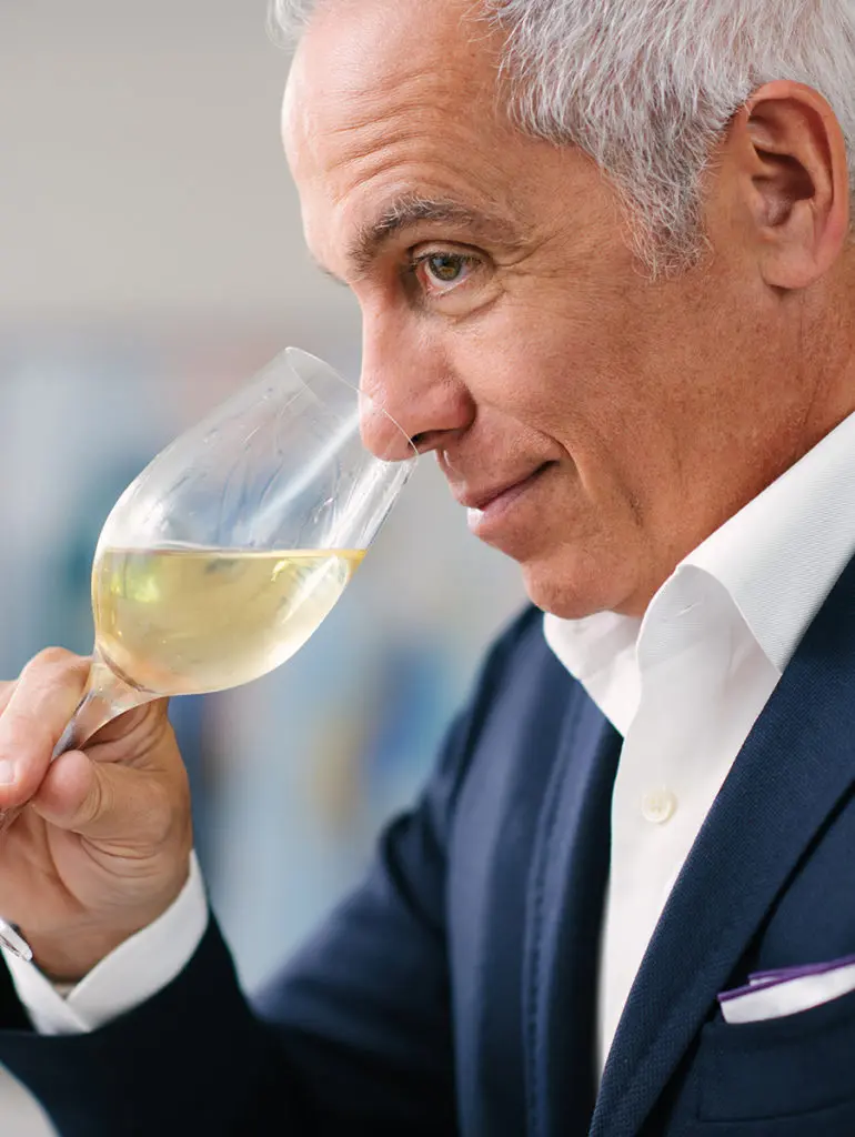 A photo of Geoffrey Zakarian tilting a glass of wine towards his nose and smelling it.
