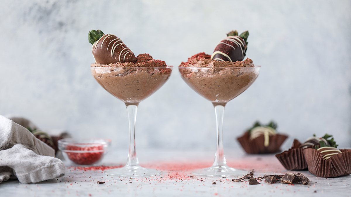 Chocolate mousse in two glasses topped with chocolate covered strawberries.