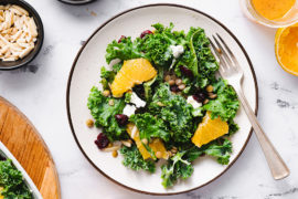 A photo of citrus kale salad on a plate surrounded by ingredients