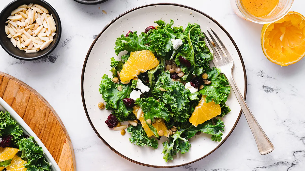 A photo of citrus kale salad on a plate surrounded by ingredients
