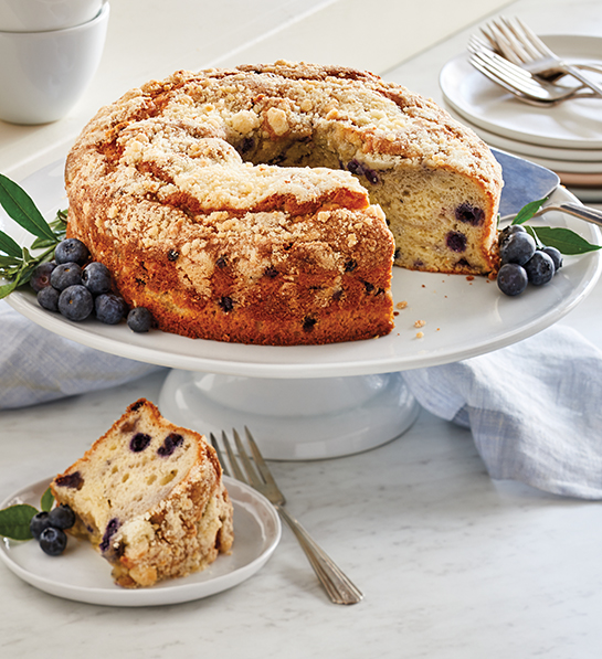 A photo of facts about blueberries with a blueberry Bundt cake on a cake stand with a slice of the same cake on a plate in front of it.