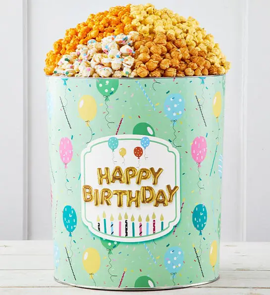 A photo of gifts for men with a tin full of different flavored popcorn covered with balloons and a "happy birthday" message.