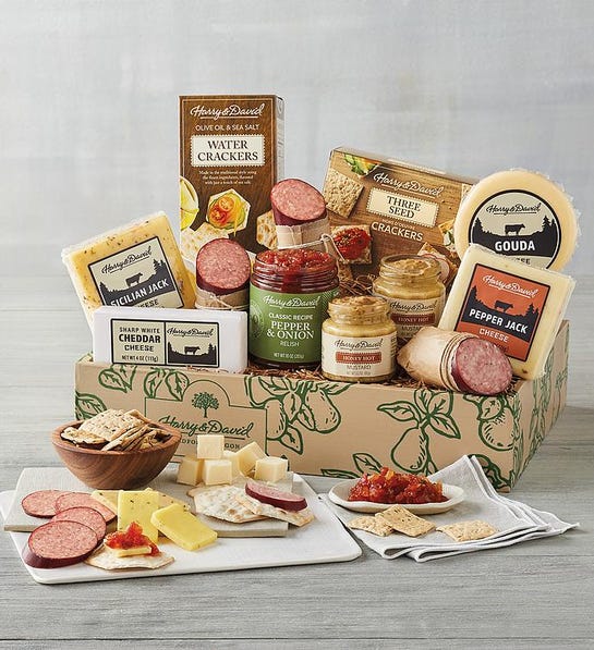 A photo of gifts for men with a box full of cured meats, cheeses, and spreads with the same ingredients on a cutting board and plates in front of the box.