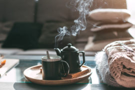 A photo of how to make tea with a pot and a cup on a plate resting on a coffee table next to a pile of blankets