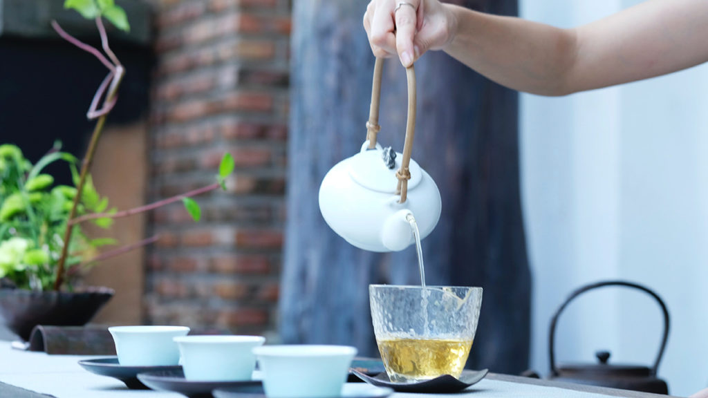 A photo of how to make tea with someone pouring tea into a glass cup.